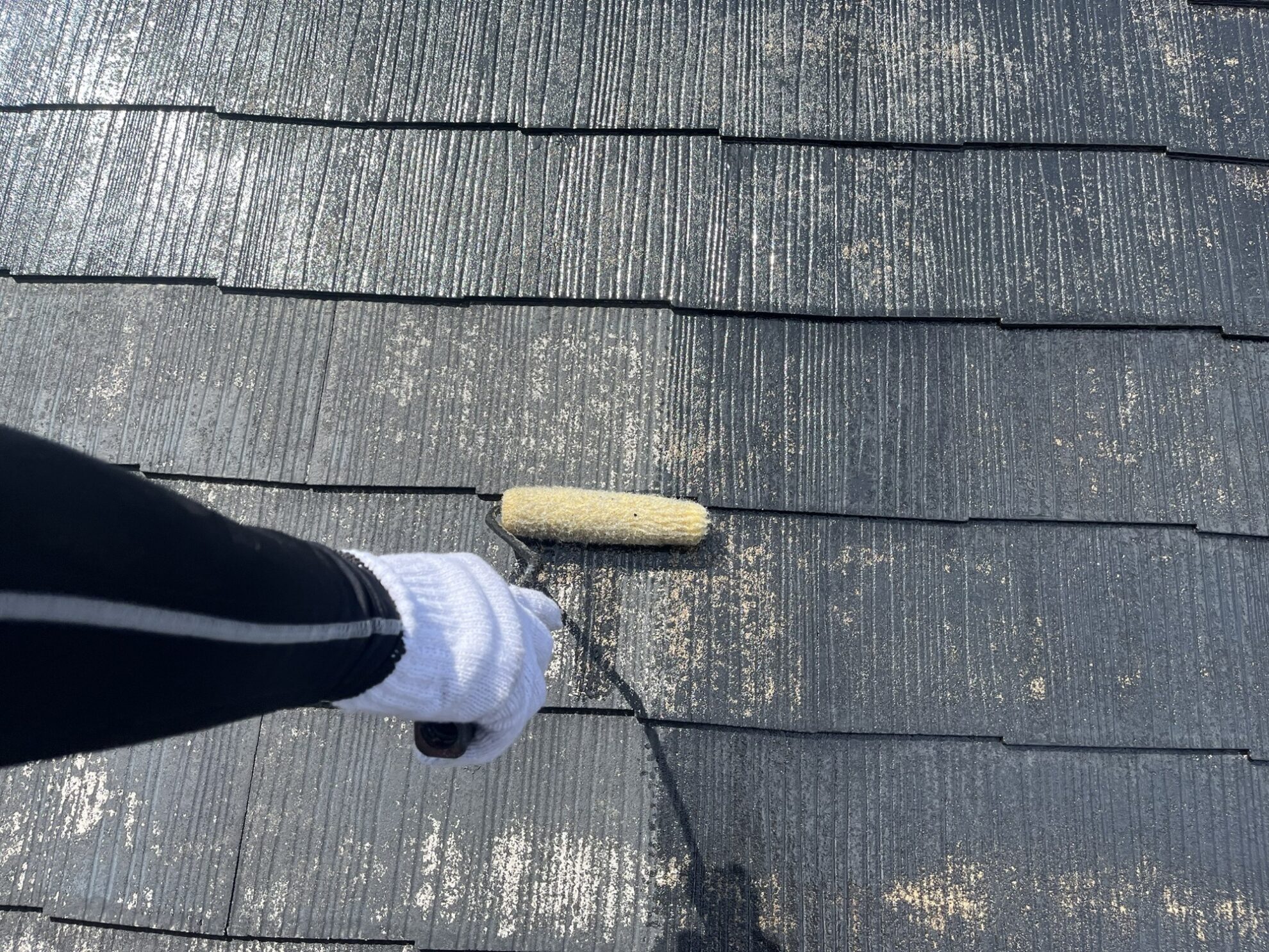 宮城県多賀城市のスレート屋根をローラーで丁寧に下塗り施工している様子。吸い込みをシーラーで止めて濡れ色になるまで塗り込んでいます。