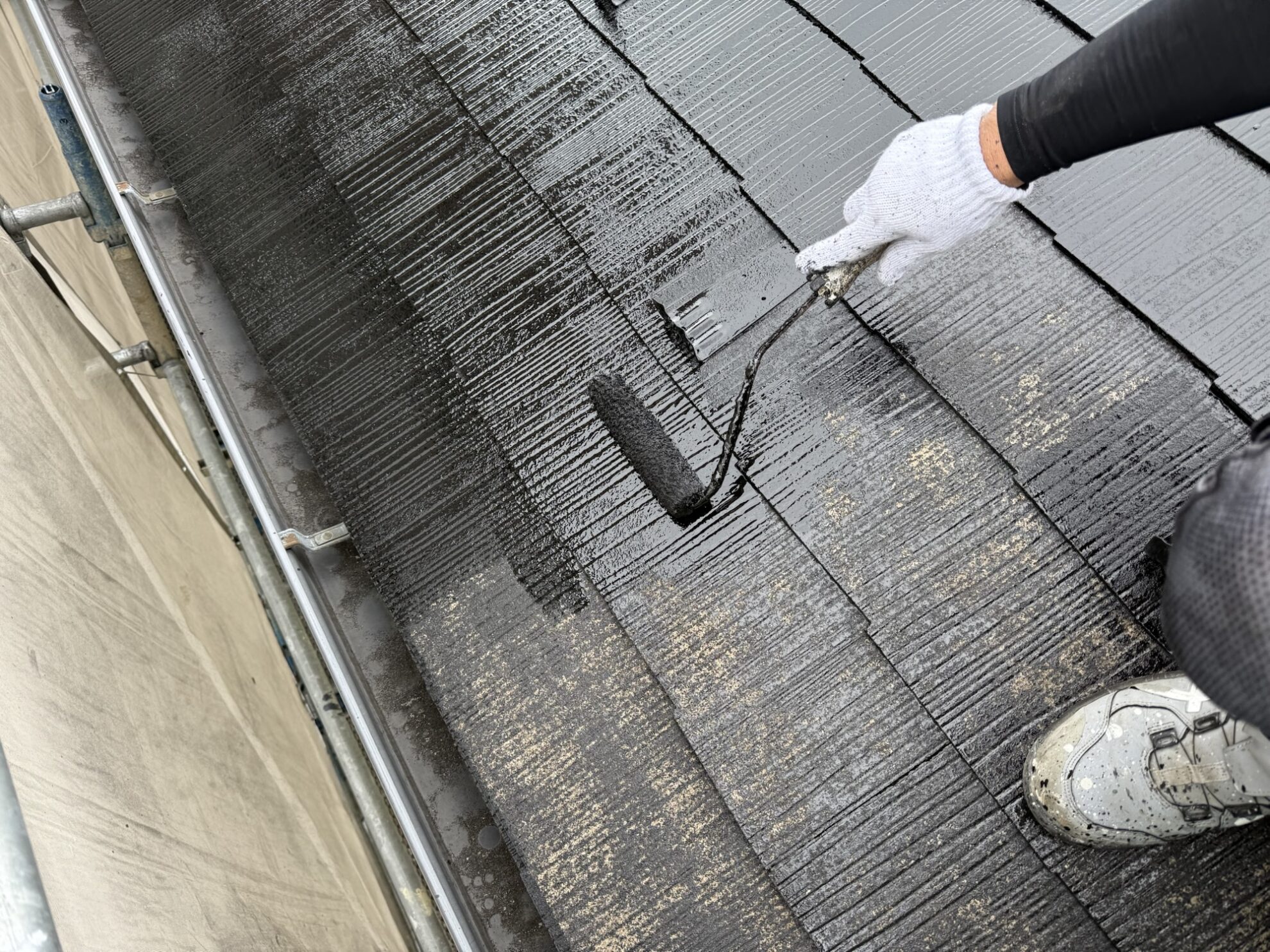 多賀城市のアパート屋根に中塗り塗装を均一に広げている作業中の様子。塗料の厚みを均一に整えています