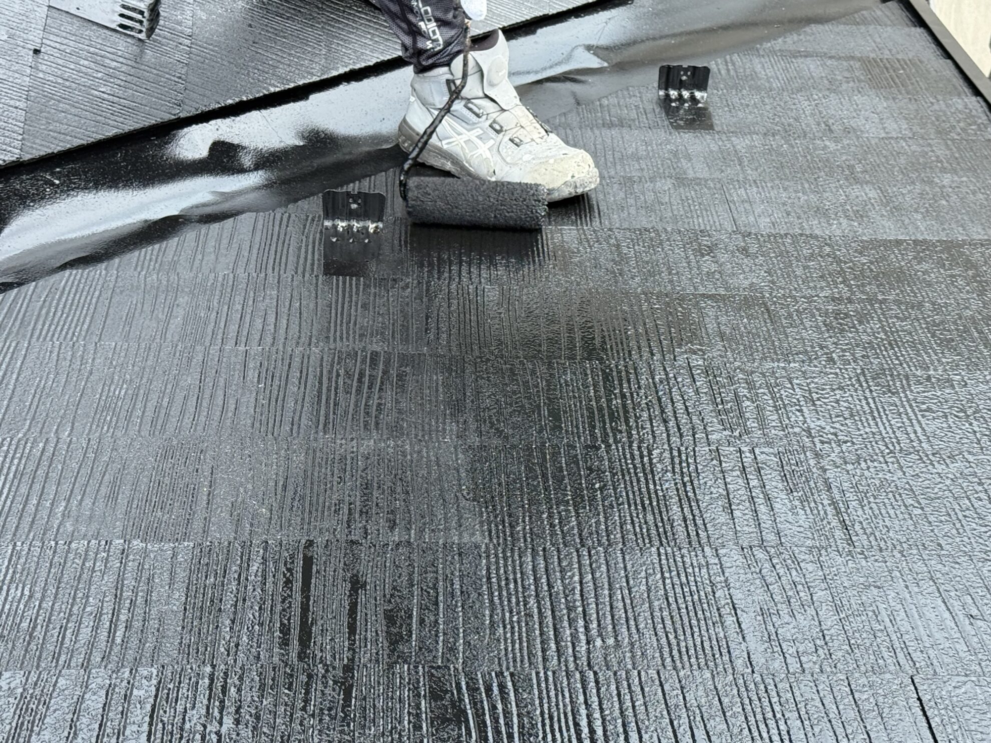 賀城市 アパート屋根塗装 上塗り作業中｜職人がローラーで丁寧に塗膜を仕上げている様子